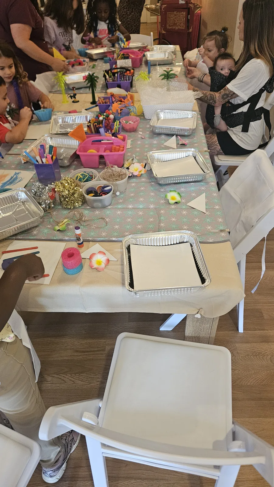A long STEAM Sprouts craft table prepared with paint, trays, markers, yarn, and children’s in-progress projects